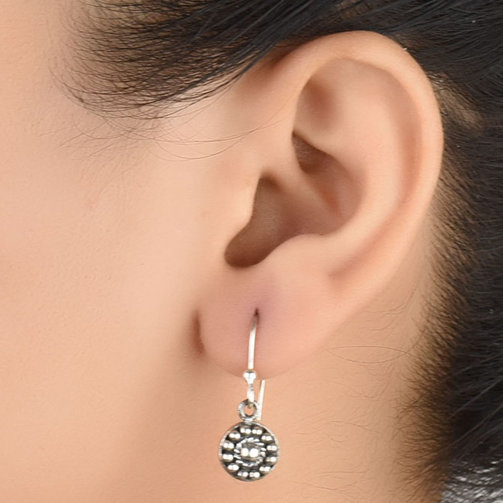 Side angle showing engraved circle pendent drop earrings with silver tones.